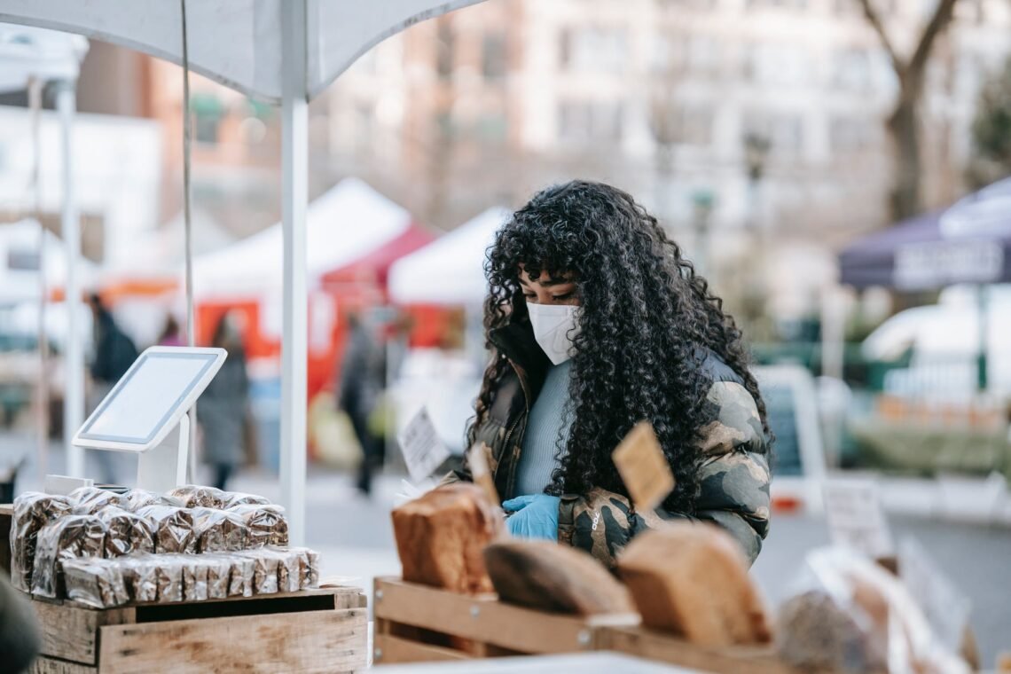 black woman in mask choosing food in street bakery