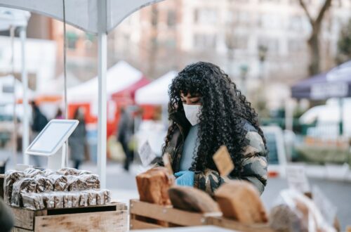 black woman in mask choosing food in street bakery